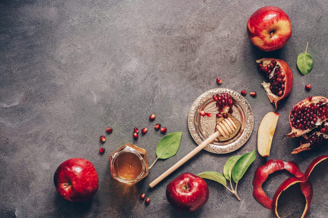 Apples, pomegranate and honey on a dark rustic background. Traditional Jewish food. New Year - Rosh Hashanah. Top view, copy space, flat lay.